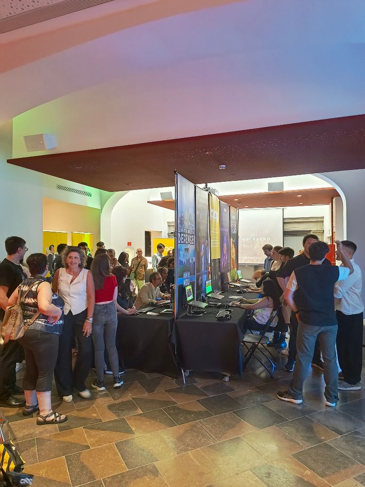 Fotografía mostrando la parte de videojuegos del evento, con gente hablando y probando los diferentes proyectos.