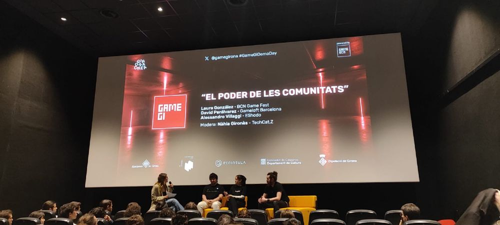 Fotografia mostrando los ponentes Laura González, David Perálvarez y Alessandro Villaggi, y a la mediadora Nàhia Gironès, con el título visible en la pantalla "El Poder de les Comunitats".