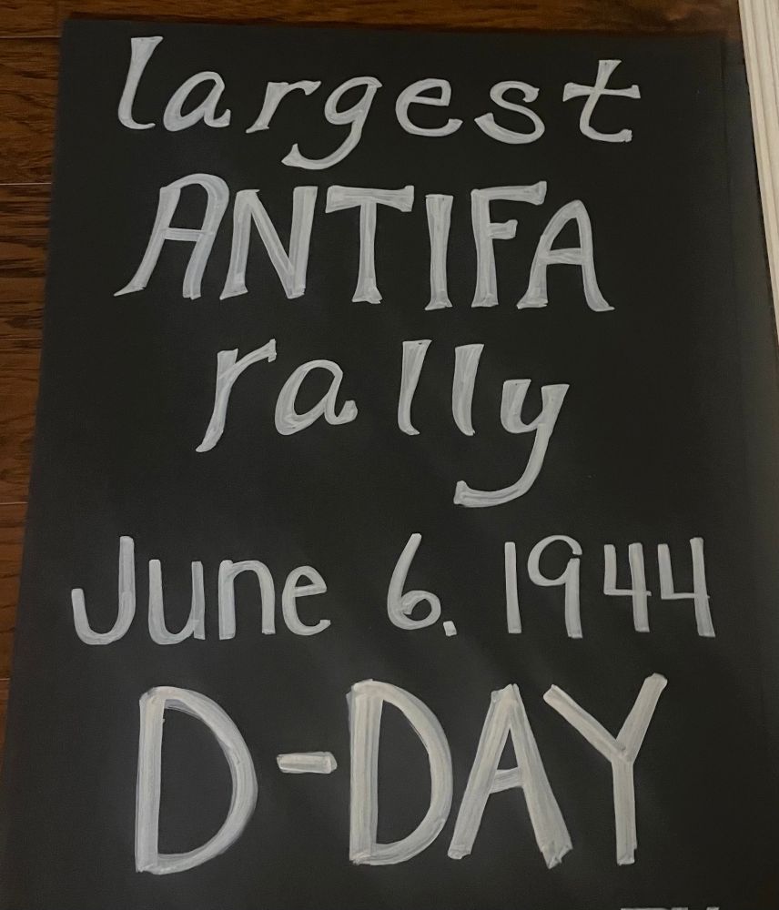 Black poster with bold white writing that’s says “largest Antifa Rally June 6, 1944 D-Day.”