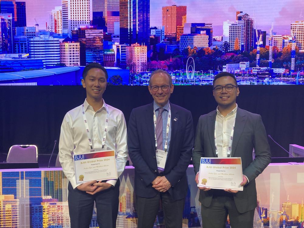 Three people posing for a photograph. The outer two holding up certificates.