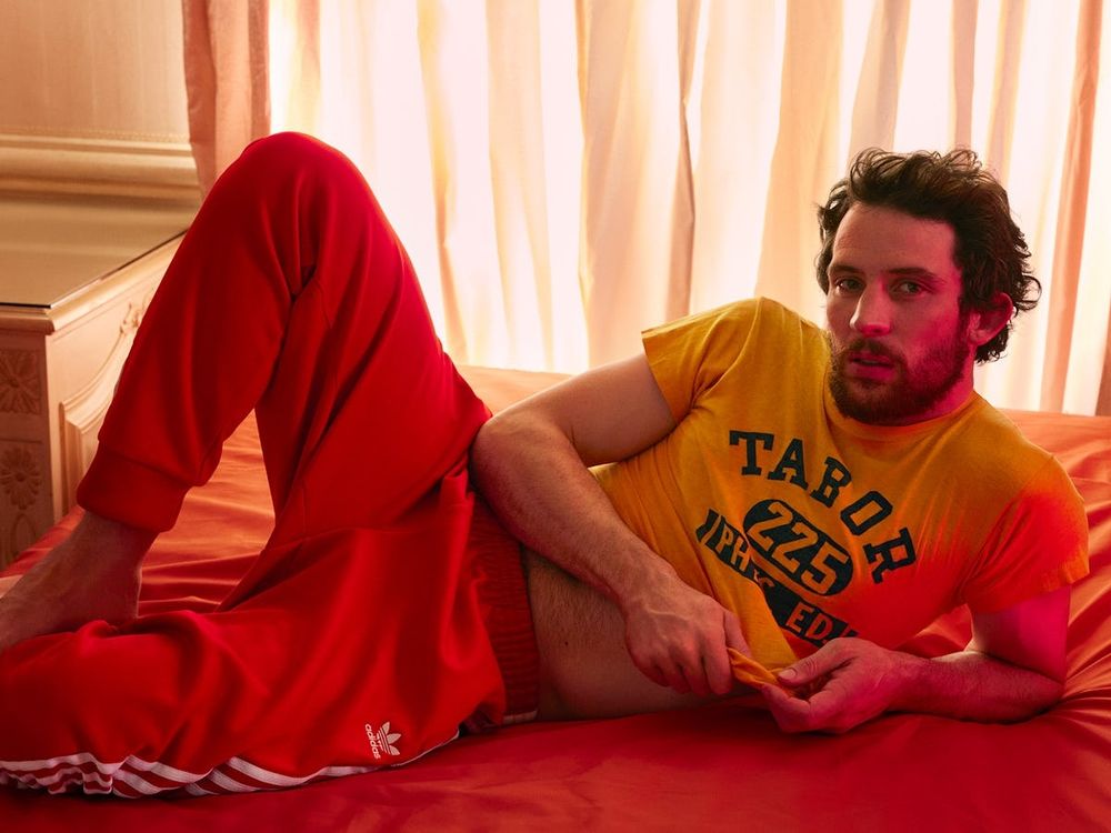 Josh o'connor en una fotografía editorial, con un crop top amarillo y pantalones de chándal.