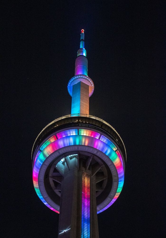 Closeup of the CN Tower at night lit in rainbow colours