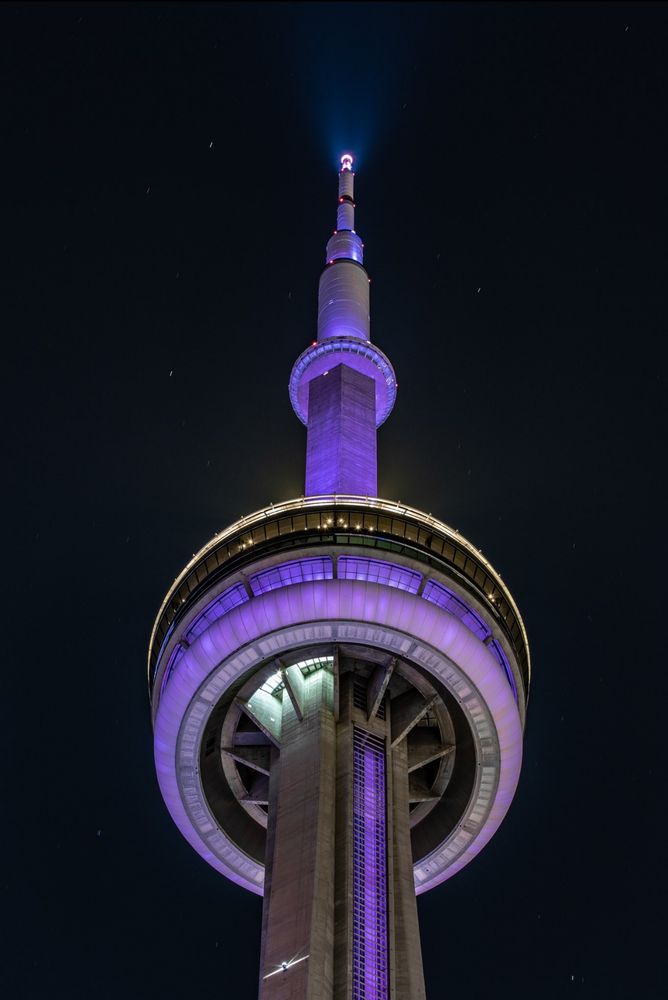 Closeup of the CN Tower at night lit purple / Gros plan de la Tour CN illuminée en violet la nuit.