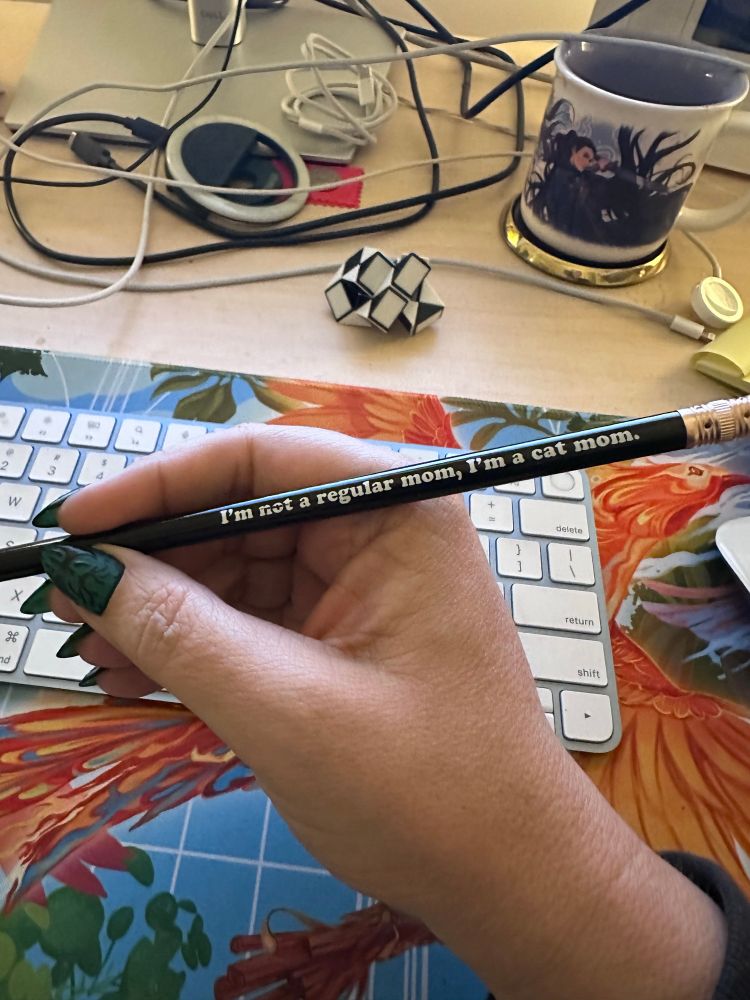White woman’s hand holding a pencil that says “I’m not a regular mom. I’m a cat mom.”