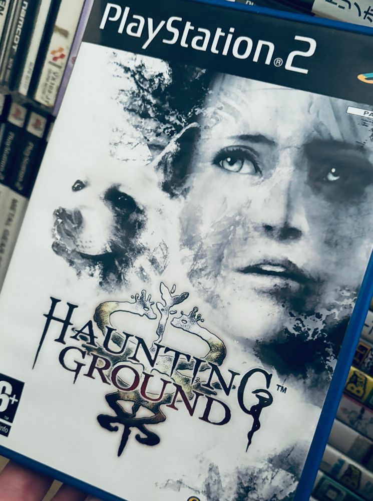 A photo showing the box for Haunting Ground (PlayStation 2) held up to the camera. The cover is almost monotone, with the heroine and her faithful dog’s face taking up most of the space. They’re rendered in a hazy manner with no easily defined edges.