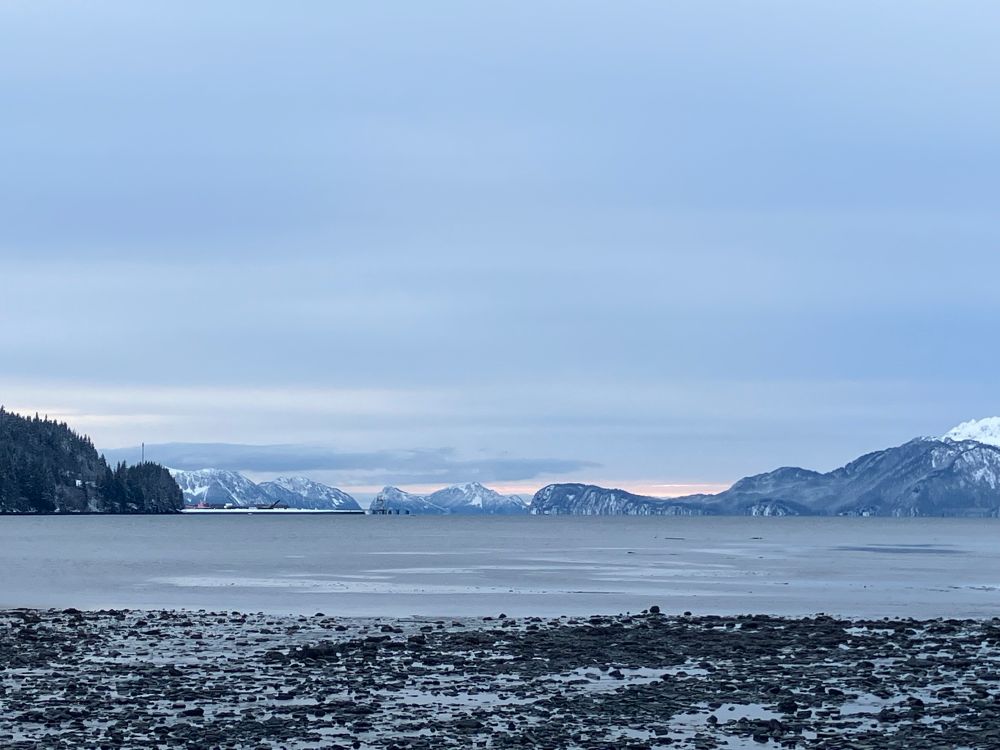 A snowy beach with headlands and alpen glow in the distance