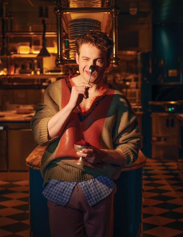 A photo of Kit Connor looking adorable, he's holding a spoon up to his nose. 
