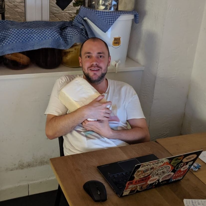 Me holding a 3kg block of fresh butter wrapped in paper. Sitting in front of a laptop covered in stickers.