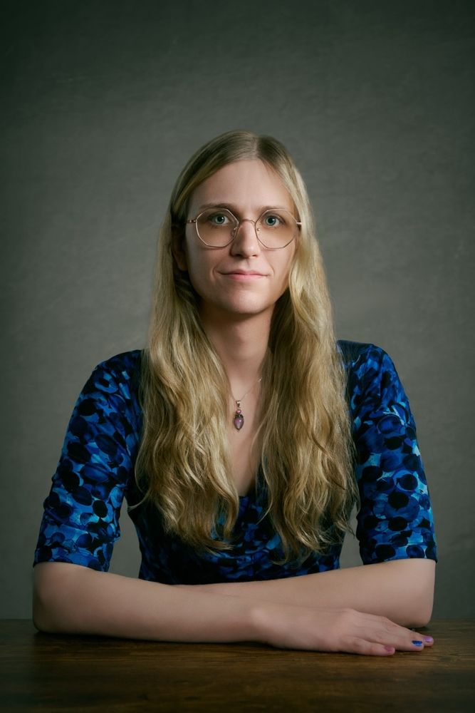 A professional headshot of me sitting at a desk wearing a blue dress. (My favorite part here is that my nails are blue and pink alternating, and I'm wearing a blue dress with a pink necklace. And they just happen to match perfectly!)
