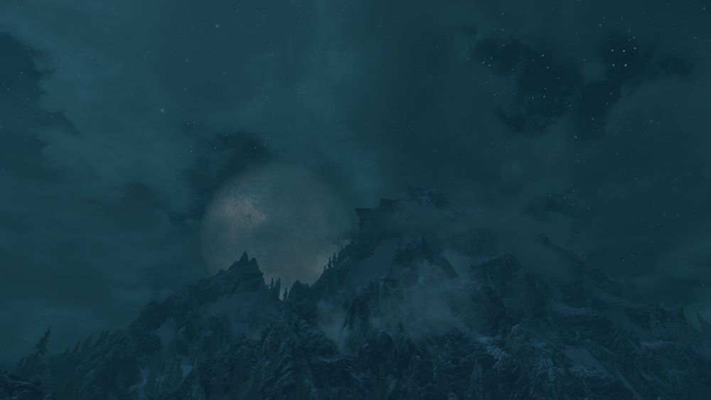 A screenshot of unmodded Skyrim at night; Masser, the largest of the two moons, is in full phase where it is peeking out from behind the Whiterun mountain tops, surrounded by nighttime clouds and stars.