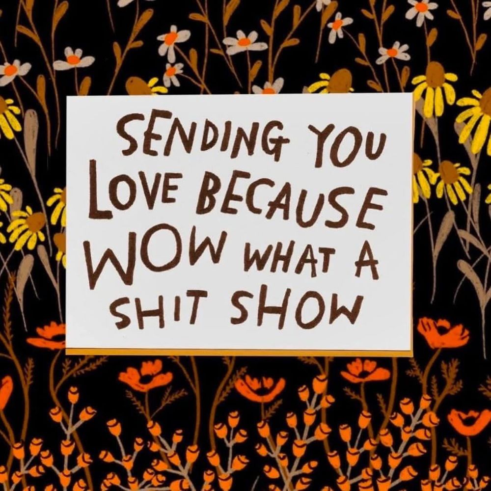 An image of flowers on a black background, in front, a white card with brown sans serif letters that say, “Sending you love because WOW what a shit show,”