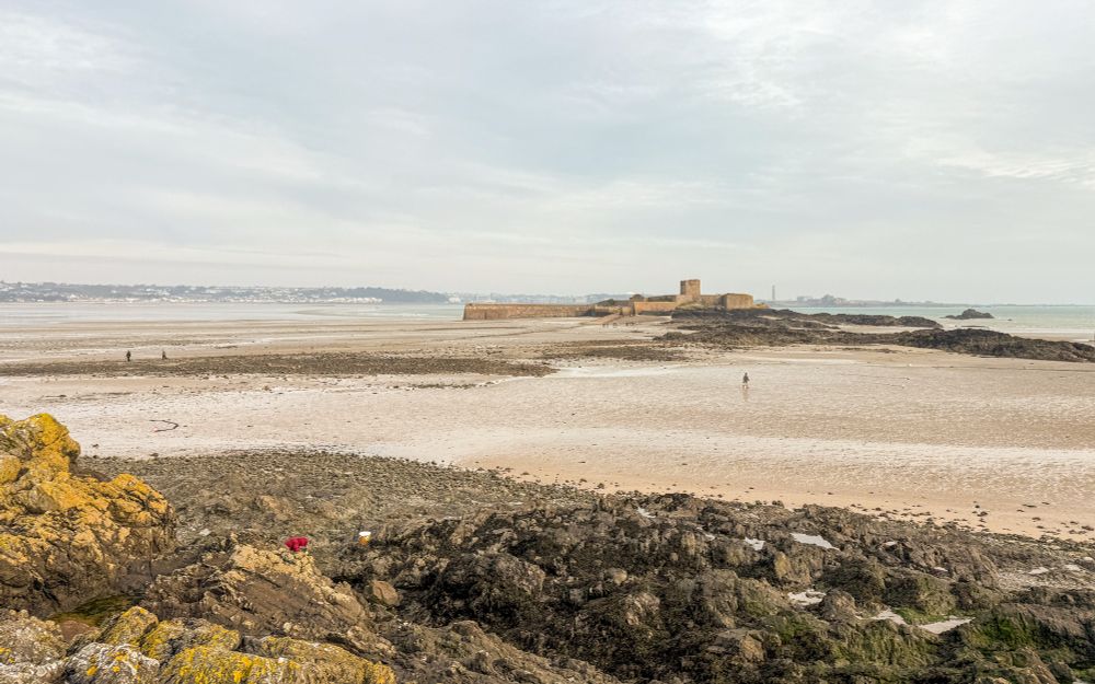 A view of rocks and sandy beach. There is a tower in the distance. 