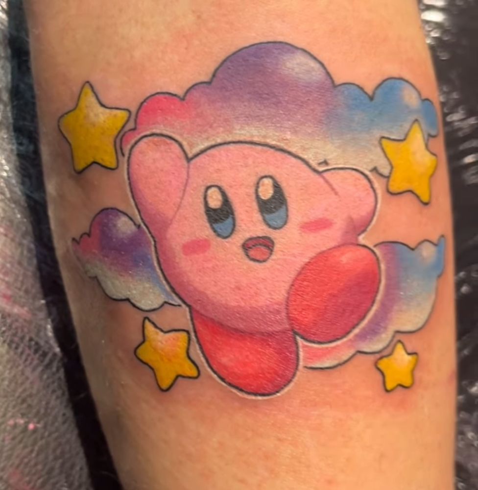Kirby tattoo. Kirby is surrounded by three colourful clouds and four yellow stars. 