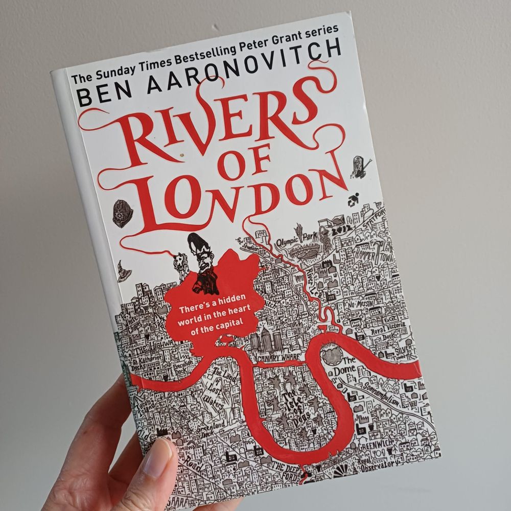 a colour photo human hand holding up a paperback copy of Rivers of London by Ben Aaronovitch 