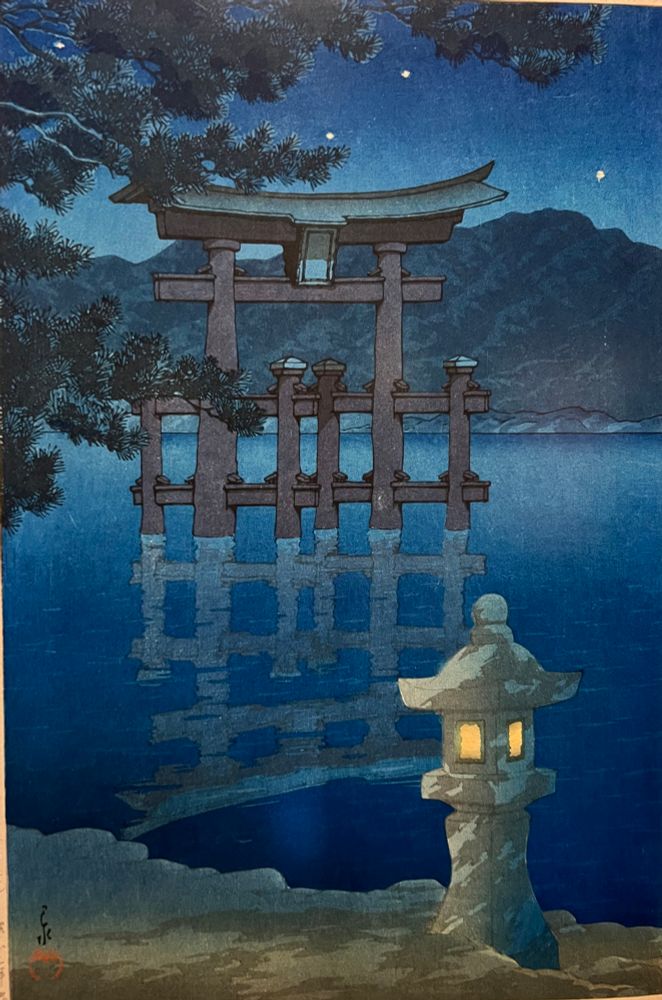 Der Tori von Miyajima spiegelt sich bei Nacht im Wasser, im Vordergrund eine beleuchtete Steinlaterne