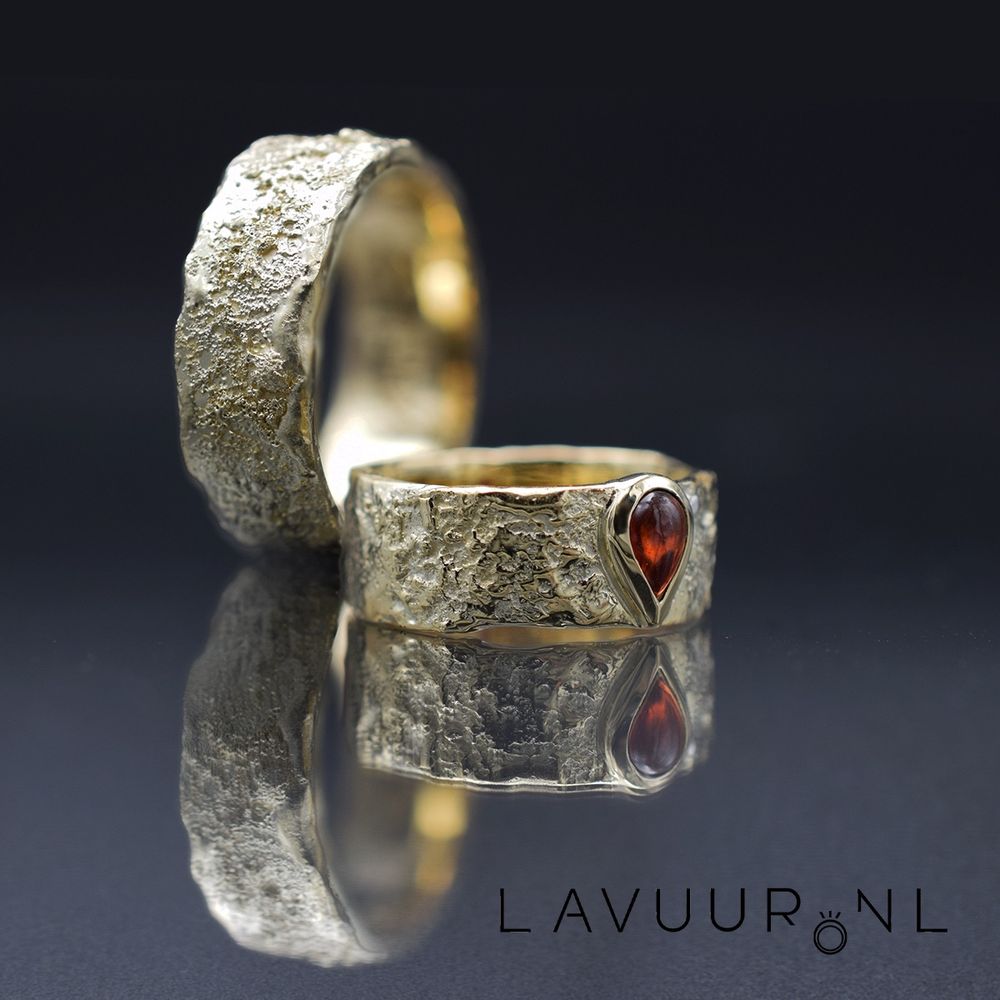 Handgemaakte ruw gedecoreerde gouden trouwringen, waarbij in één van de ringen een druppelvormige rode granaat is gezet