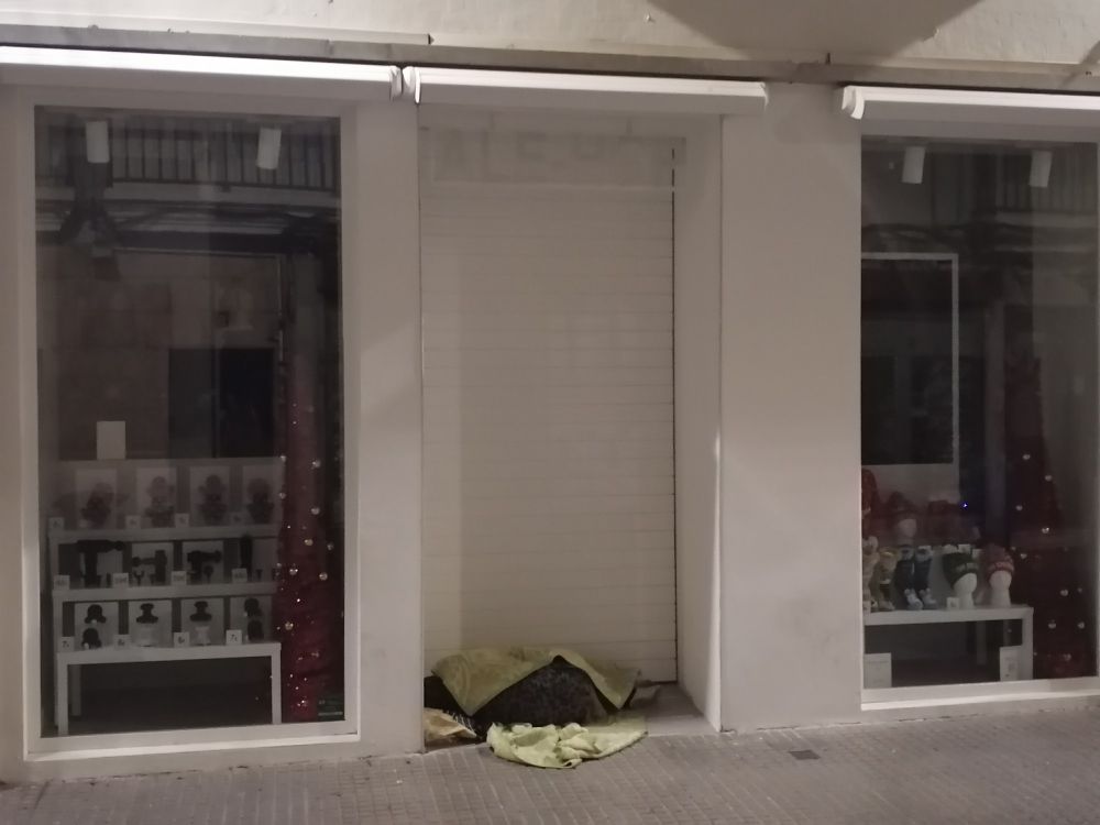 Una persona duerme en la madrugada a la intempèrie en una calle comercial de Cádiz. 