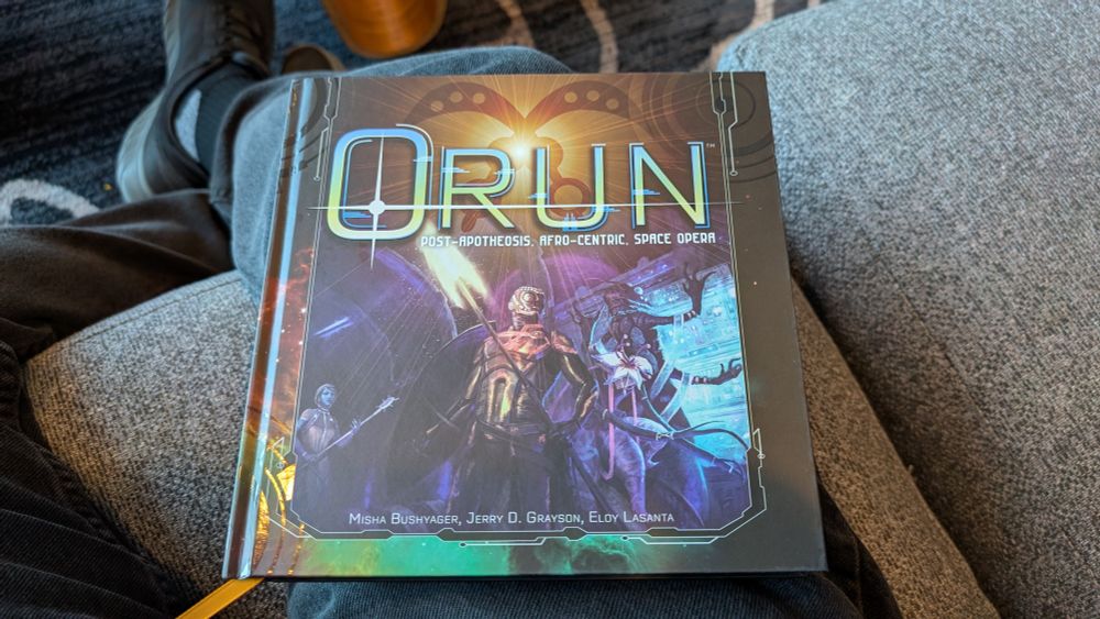 Cover of the Orun rulebook depicted several alien species including one heavily inspired by African aesthetics in the center holding what appears to be a weapon with a spearhead made of light.