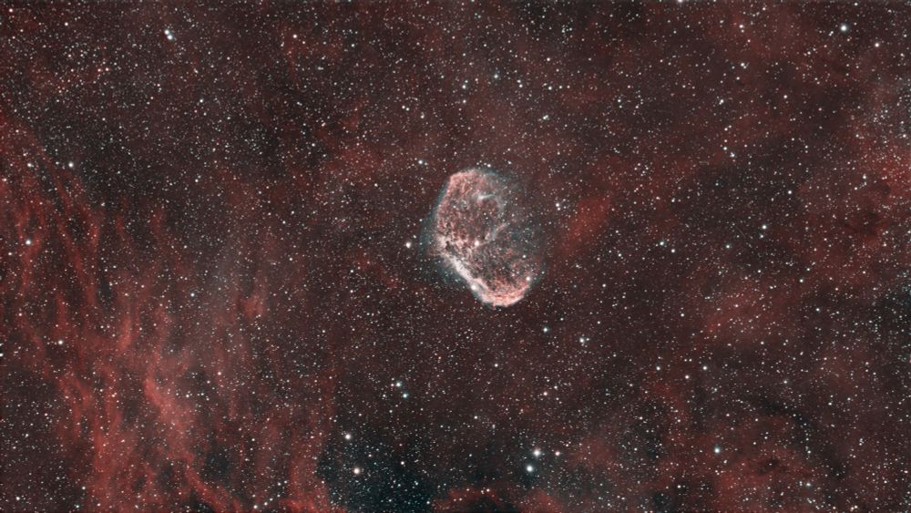 A brain-like structure of gas and dust is in the centre, with red gas and stars dominating the whole image in the background. 
