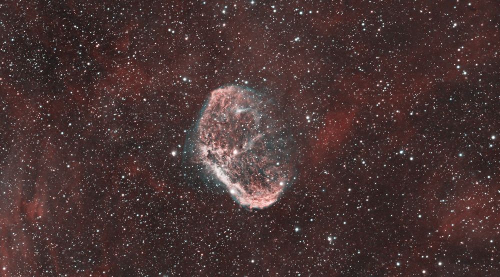 A close up of the brain-like structure of gas and dust is in the centre, with red gas and stars dominating the whole image in the background. 