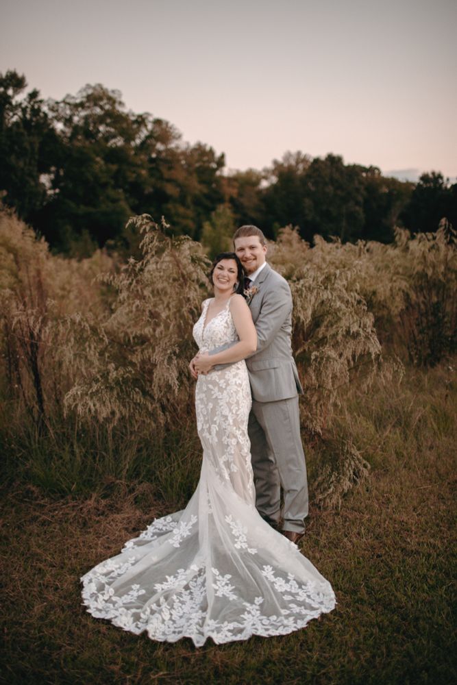 My husband and I standing in a field on the farm where we were married, with the train on my wedding dress in front of us.