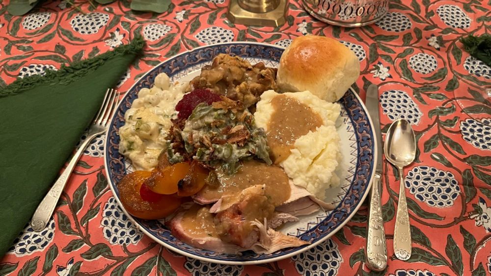 A full Thanksgiving plate, with cranberry sauce, mashed potatoes and gravy, green bean casserole, creamed pearl onions, turkey and gravy, curried fruit, stuffing, and a roll.