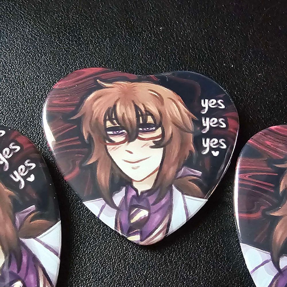 A photo of a pinback heart button of Iwamine Shuu from Hatoful Boyfriend, in his human form. His tired eyes gaze towards the viewer with an unsettling smile and flushed cheeks. Next to him are the three options to reply to him with, "yes, yes, yes". The background is composed of dark, distorted swirls.