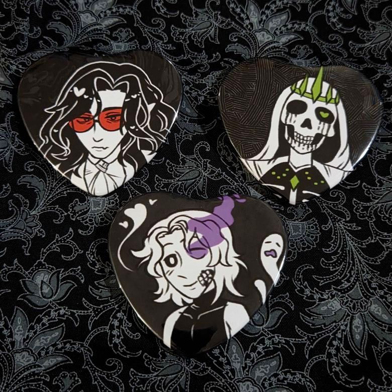 Three heart buttons illustrated in black and white with one spot color. The vampire has red lens glasses, the ghost has a purple aura flowing out from one eye, the lich has green jewelry and a heart in one eye. All of them seem interested in what they may see, in their own unique ways.