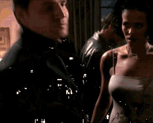 a man and a woman are standing next to each other in a room . the woman is wearing a white tank top .