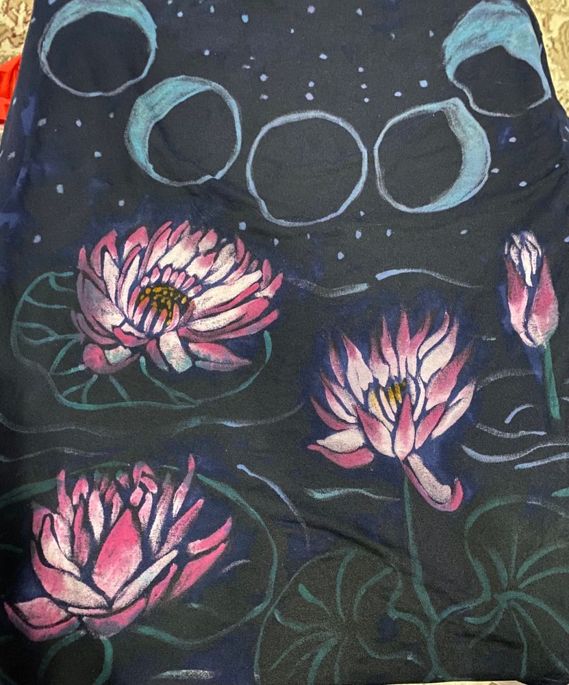 A back view of a Moon Lady T-shirt. The the little stars and the ring of moon phases around the collar are pale blue. The design below features water lilies on a background with simple lines to suggest rippling water. The lilies are painted with a simple water colour style in pink, gold and green.