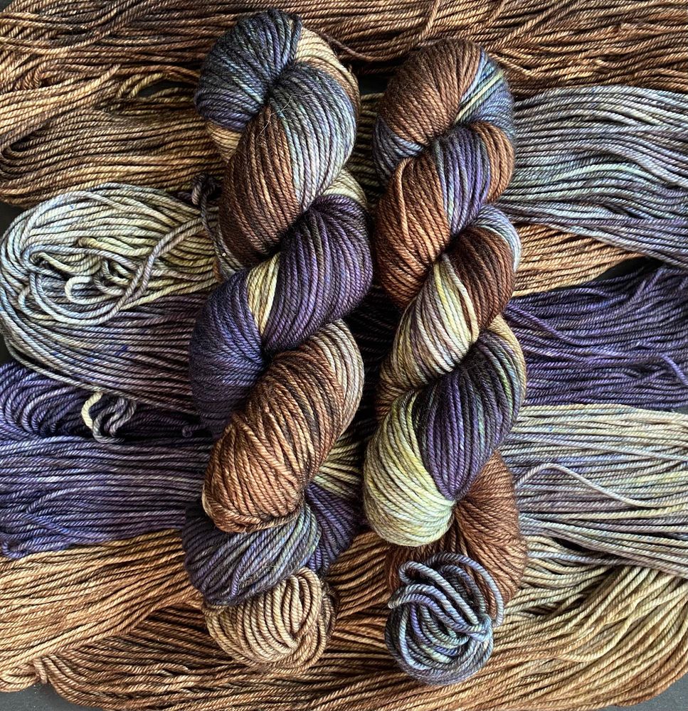 Four skeins of hand-dyed yarn in a colorway called Elisabeth’s Grey. There are elements of deep slate grey, blue-gray, brown, and gold.