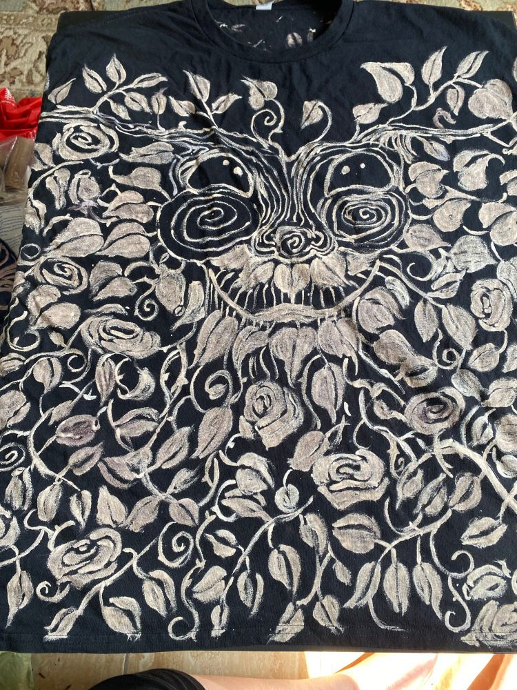 The front of a hand-painted T-shirt, size 3XL, featuring a cheerful Green Man face surrounded by leaves, thorny vines and roses.