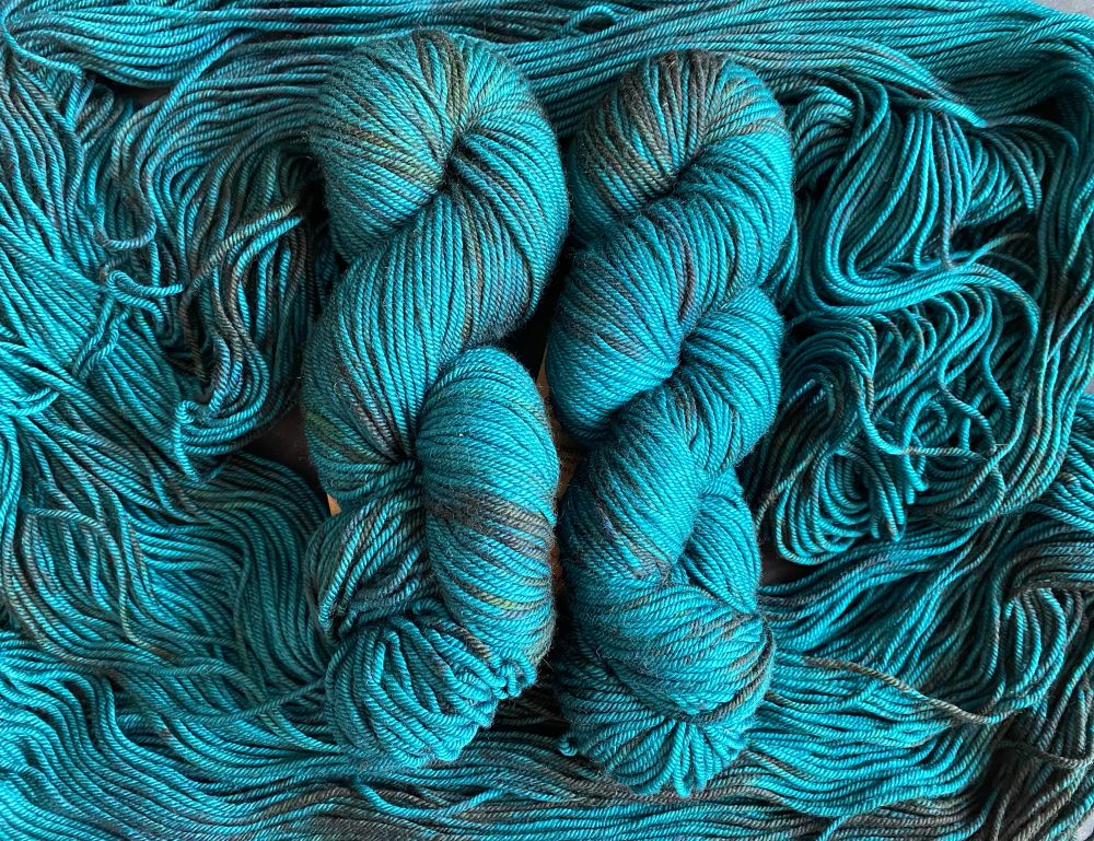 Four skeins of hand-dyed yarn in a colorway called Blackened Jade. The main body of the skeins are a rich dark teal green, with flashes of a green so dark that it appears black.