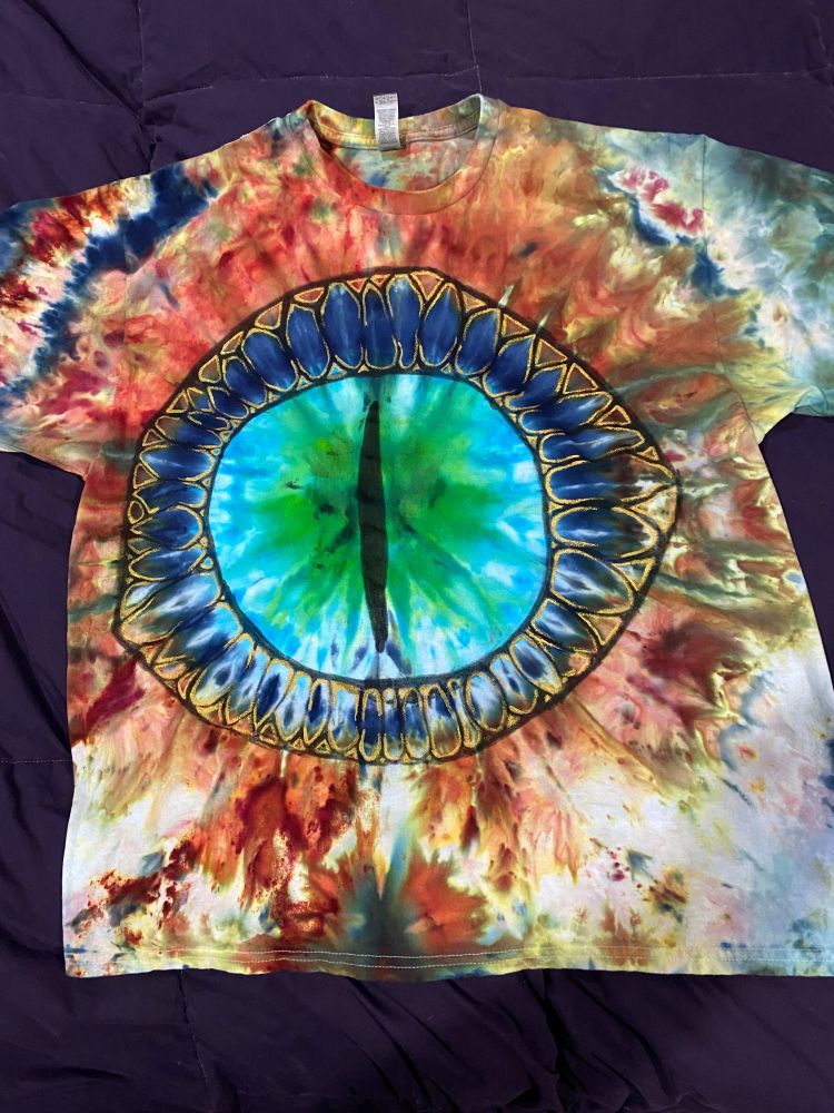 A hand-dyed and hand-painted t-shirt featuring a blue and green dragon's eye against a field of desert colors
