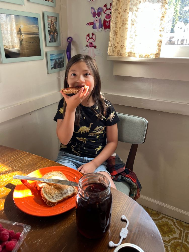 An adorable child tasting her slice of bread with peanut butter and jelly.