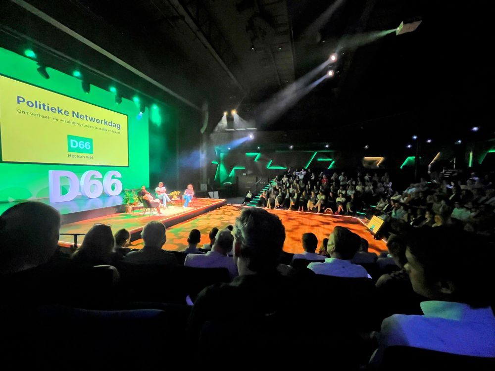 Foto van een volle zaal met op het podium Rob Jetten in gesprek met straatdokters en een wijkvertouwenspersoon voor armoedebestrijding. 
