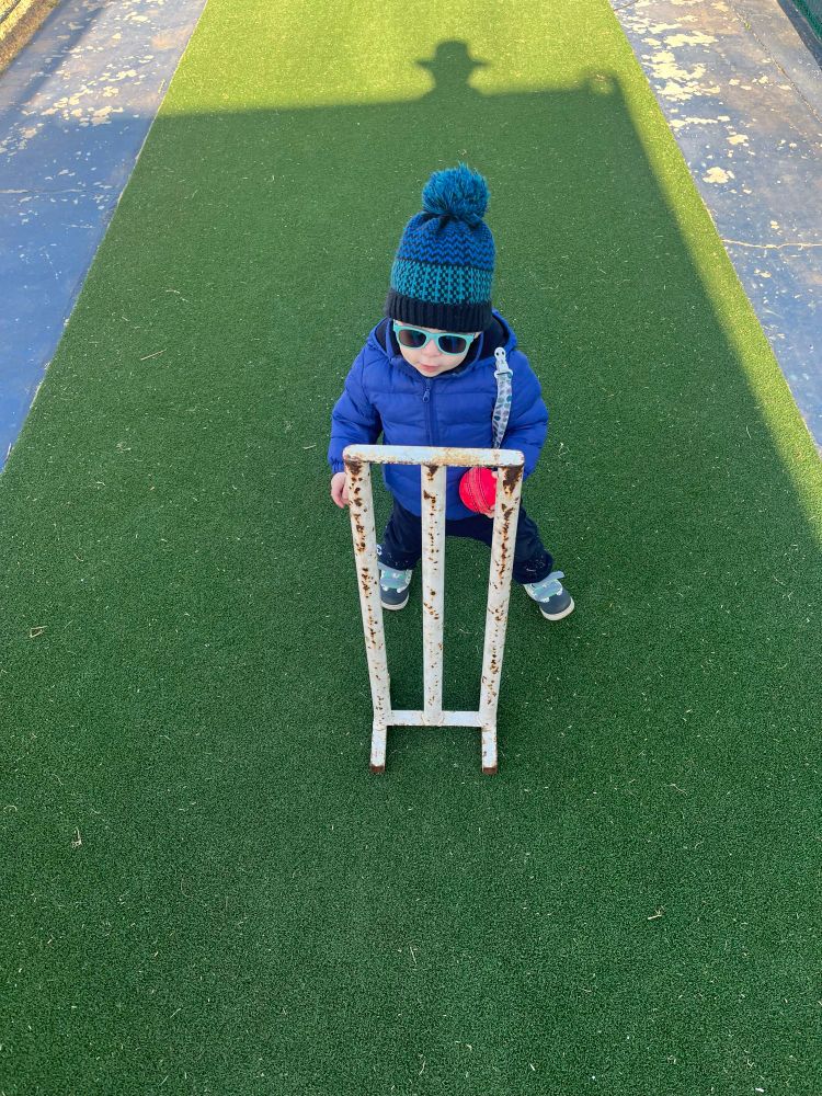 A picture of a toddler holding a cricket ball, wearing sunglasses and a beanie.