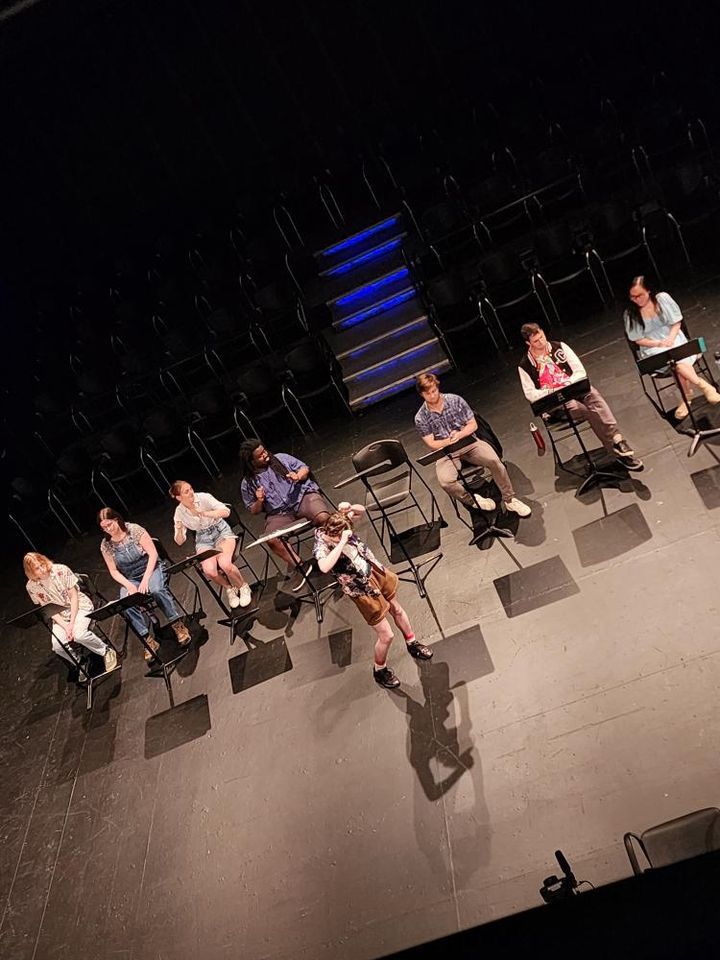 Levi dances in a blackbox theater as seven others sit and watch from behind music stands. This image is from a new work reading workshop