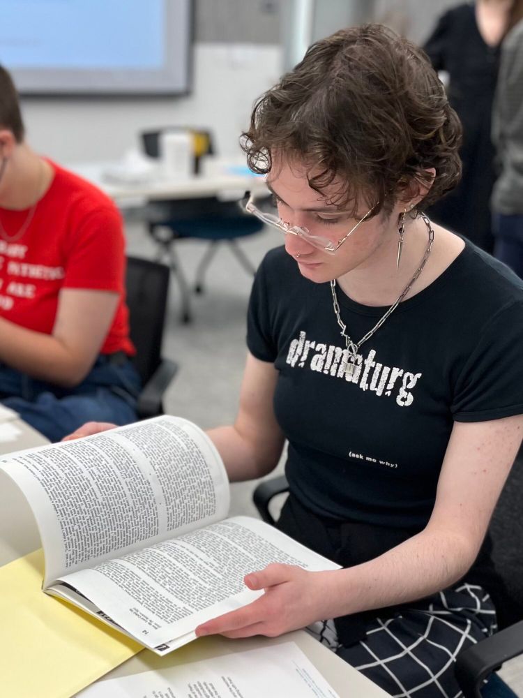 Levi is reading a book, wearing a "dramaturg" shirt.