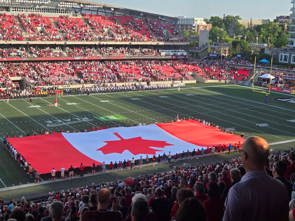 Giant Canada flag stretched out on football stadium field.