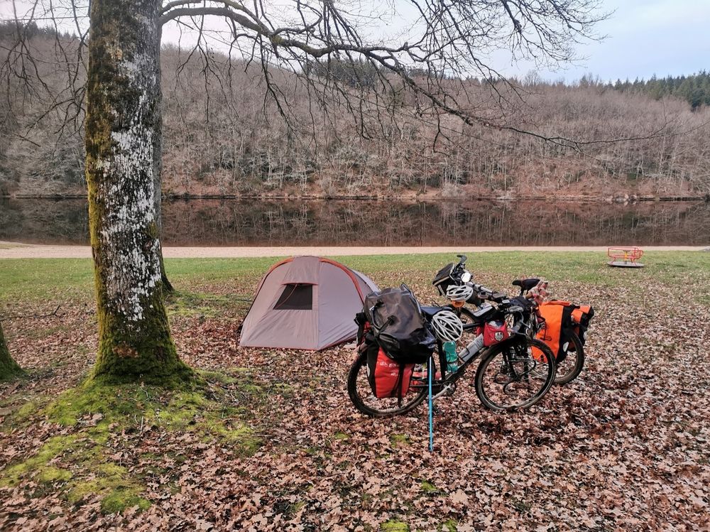 Tente et 2 vélos sur une pelouse sous les arbres, rivière au loin