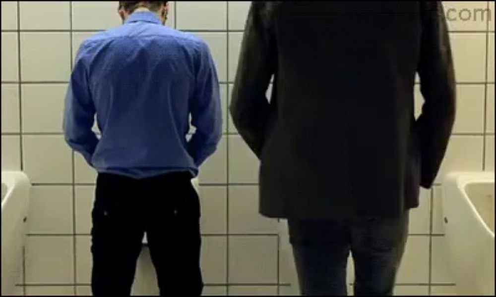 two men urinating in a public restroom with a .com logo on the corner