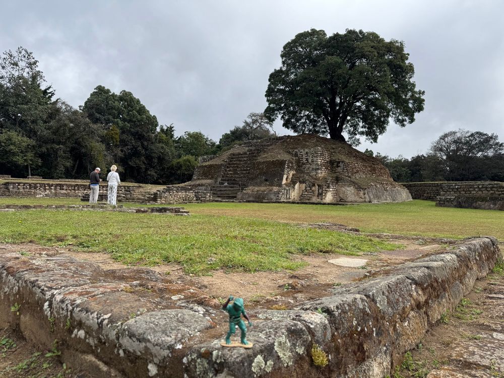 A grassy field in the foreground with trees and stone ruins including walls and small pyramids are in the background. The green Gorn action figure is near the front 