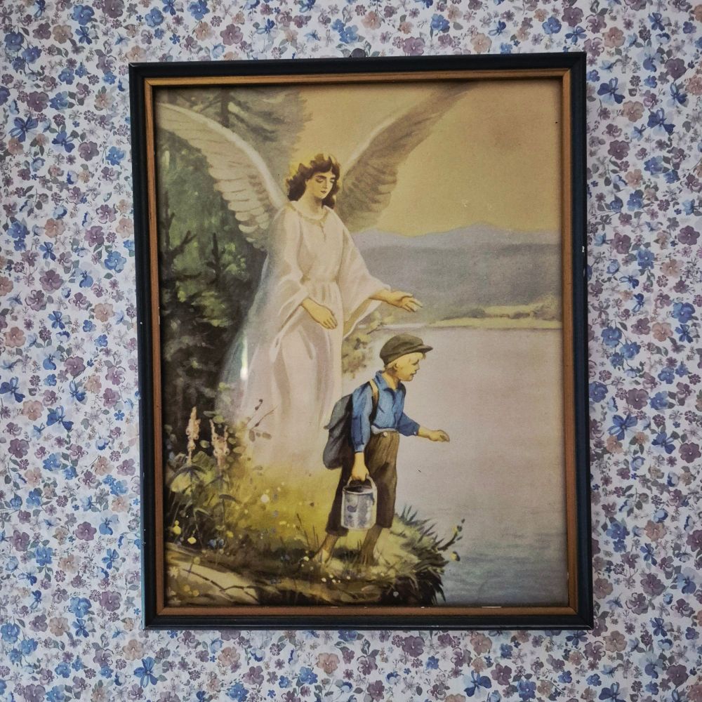A framed picture of a boy standing on a cliff's edge with a winged angel standing behind him. The angels arms are somewhat stretched out towards the boy.