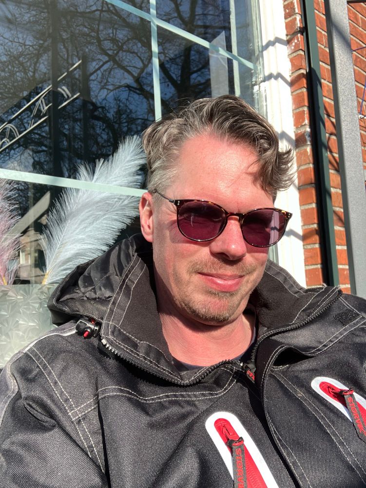 Selfie in de zon, wel met mijn zwarte werkjas aan, mijn meekleurende brillenglazen zijn donker geworden door de zon