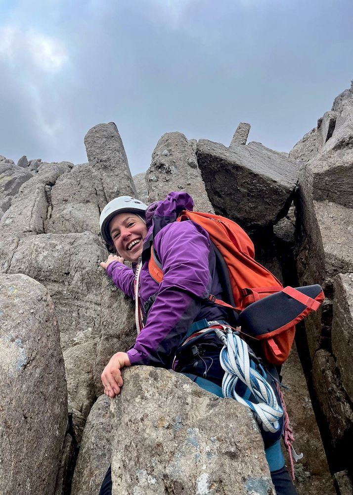 A climber mid-scrmable turns to smile at the camera.