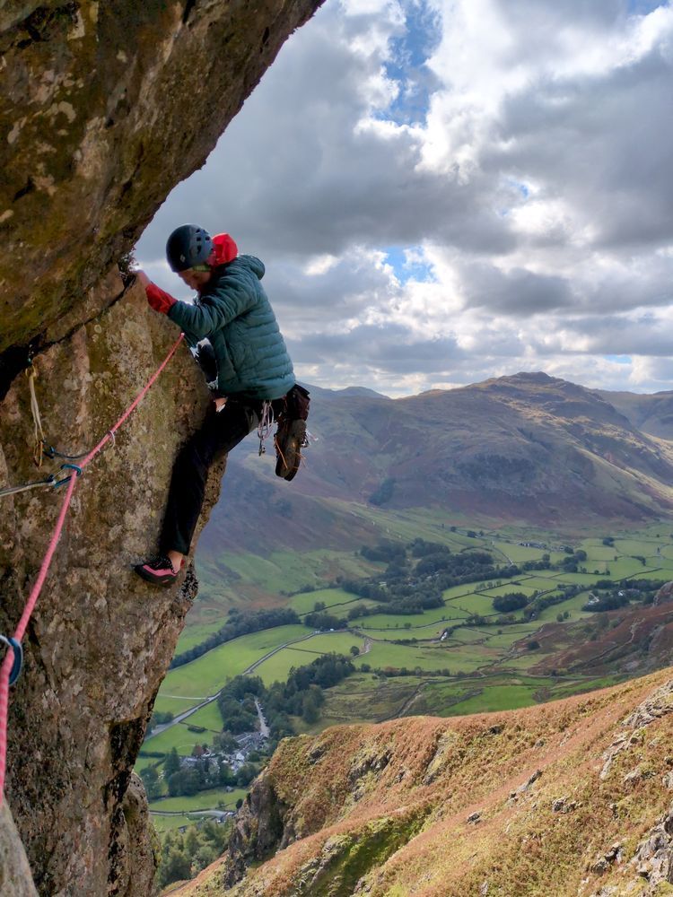 A climber surmounts a bulge on a rising traverse, a lush green valley laid out below them.