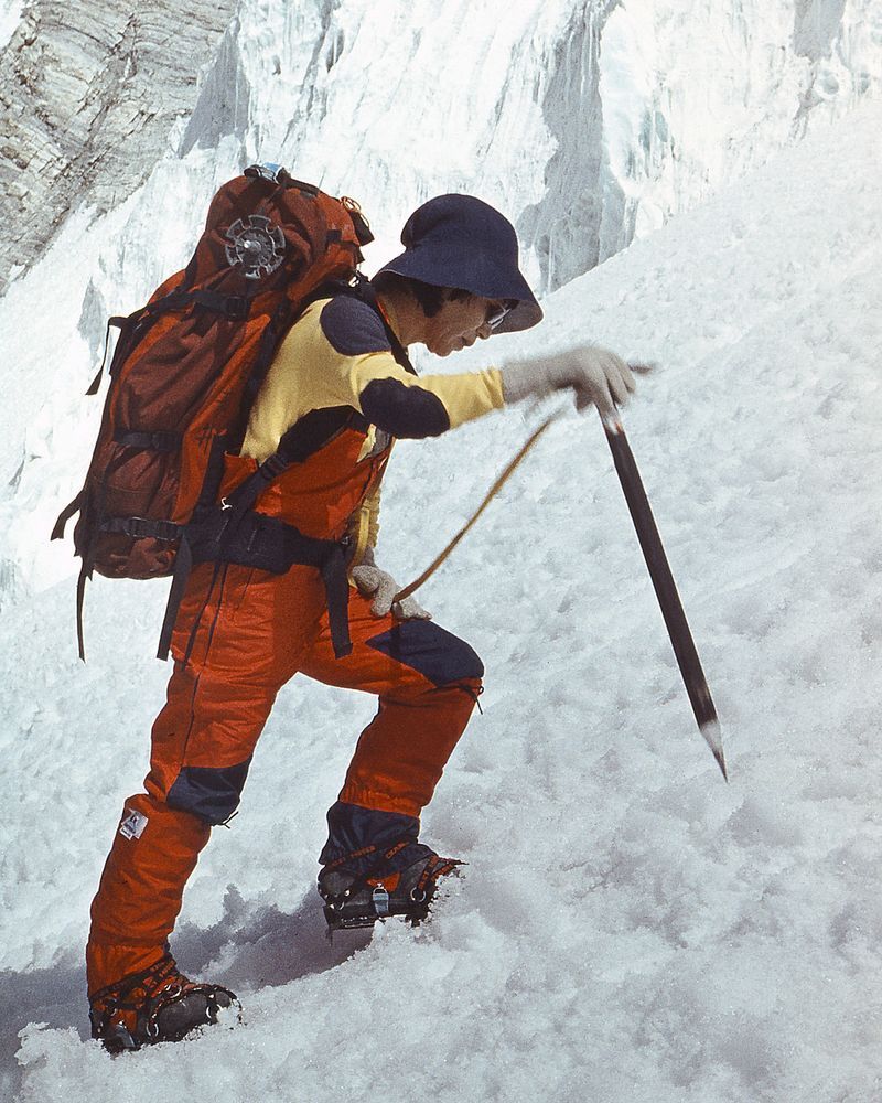 Junko Tabei, carrying a large rucksack, plunges ger walking axe into a snow slope.