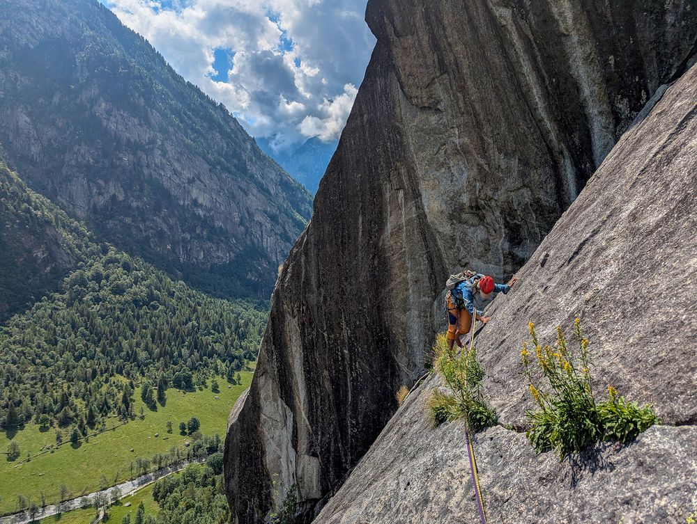 A climber traversing a thin crack on a slab above a valley and river below.