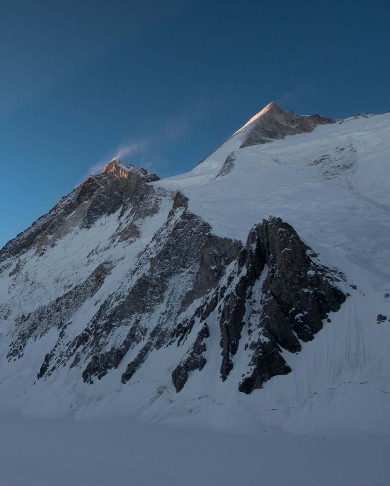 Two rocky peaks with snow blowing off their summits.